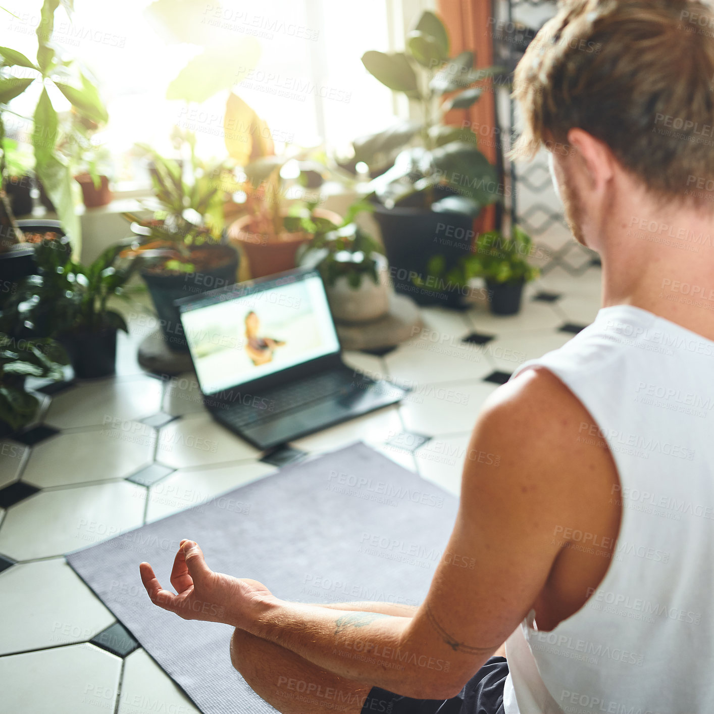 Buy stock photo Shot of a young man using a laptop while meditating in the lotus position at home