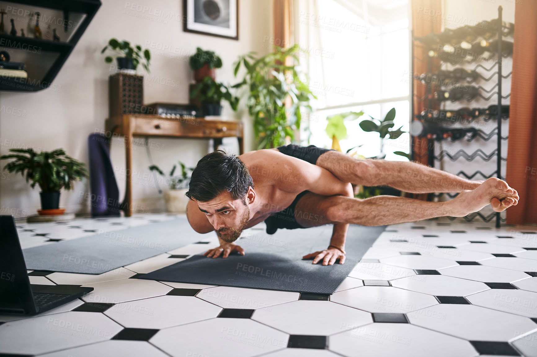 Buy stock photo Shot of a young man using a laptop while going through a yoga routine at home