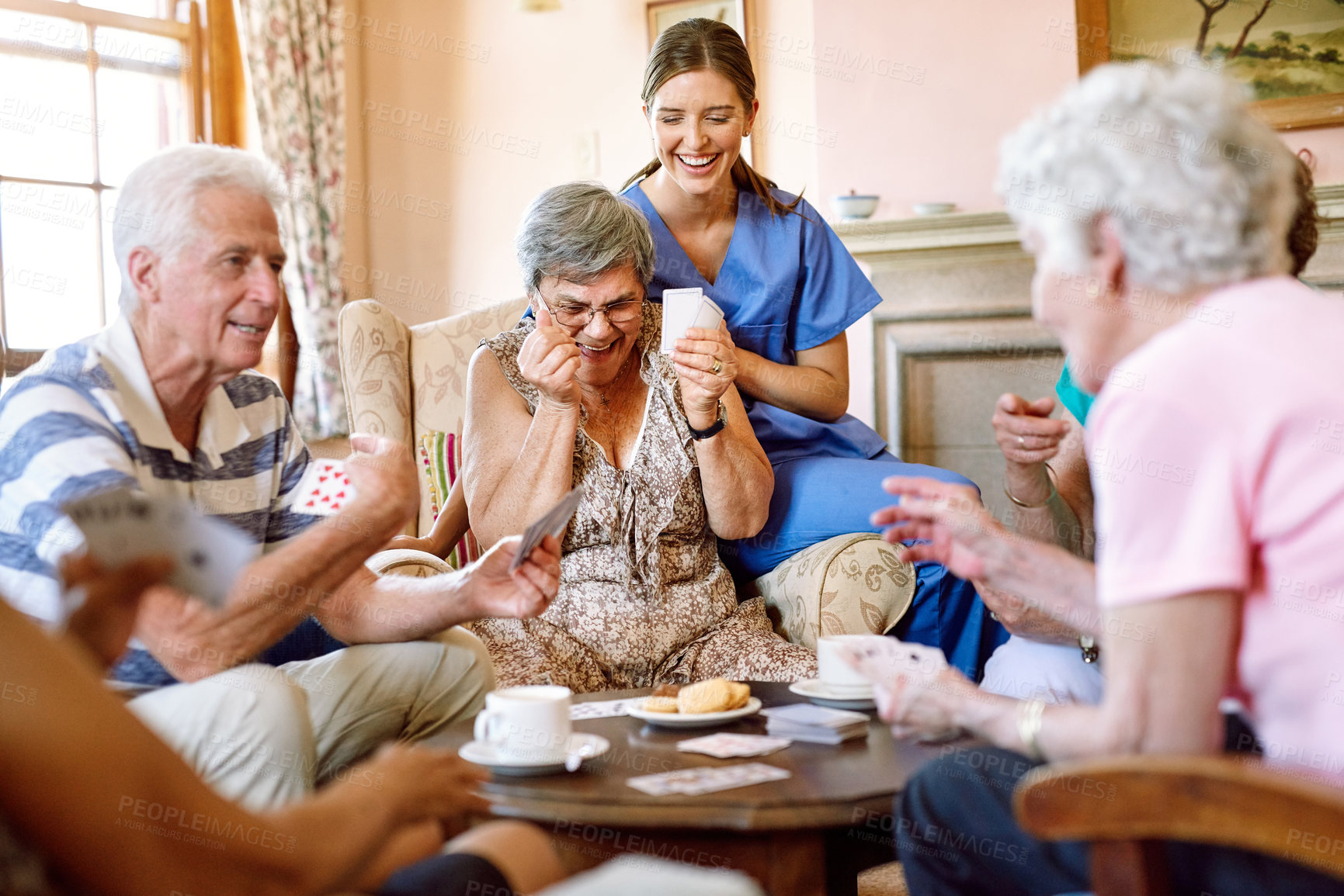 Buy stock photo Shot of a group of happy seniors playing a card game in their retirement home while a nurse watches