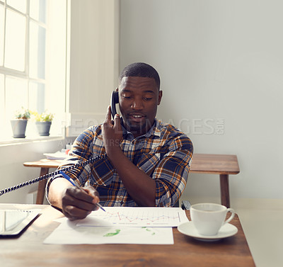 Buy stock photo Shot of a young businessman using a telephone at his desk in a modern office