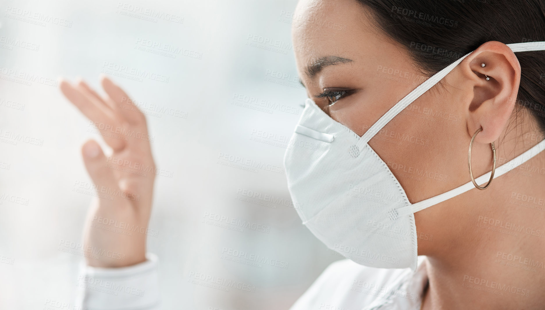 Buy stock photo Shot of a masked young businesswoman looking out of a window and waving in a modern office