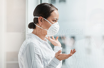 Buy stock photo Shot of a masked young businesswoman looking out of a window and talking to someone at work