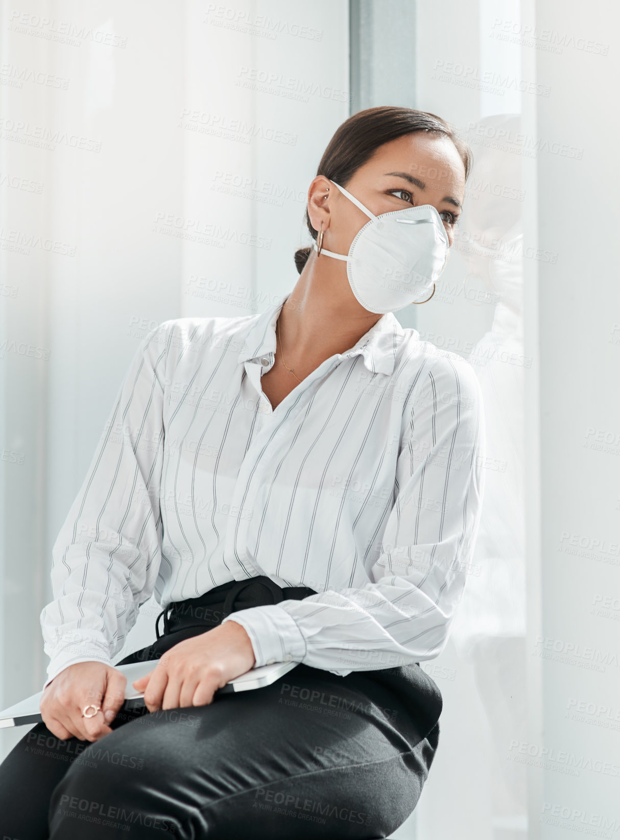 Buy stock photo Shot of a masked young businesswoman looking out of a window in a modern office