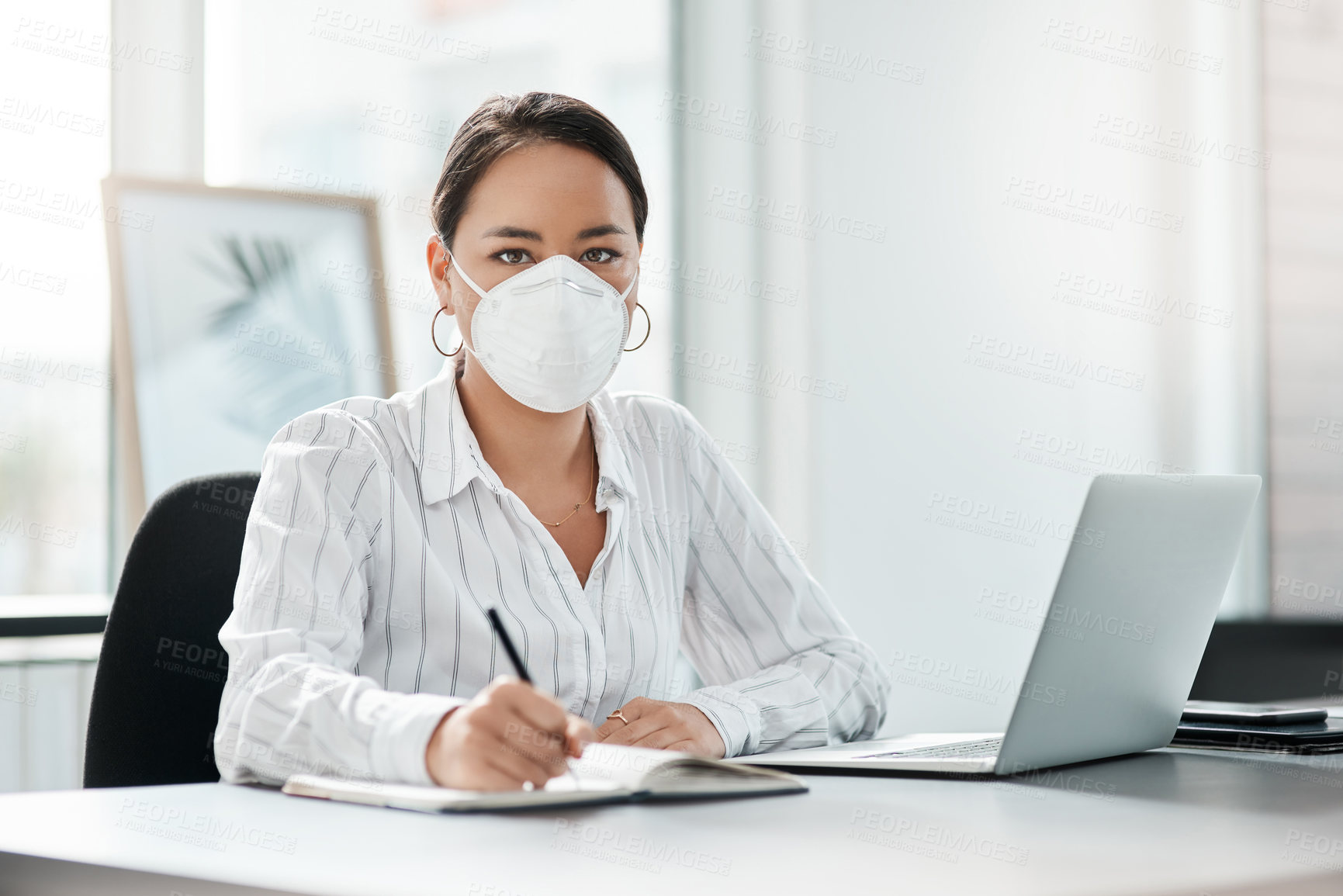 Buy stock photo Shot of a masked young businesswoman working at her desk in a modern office