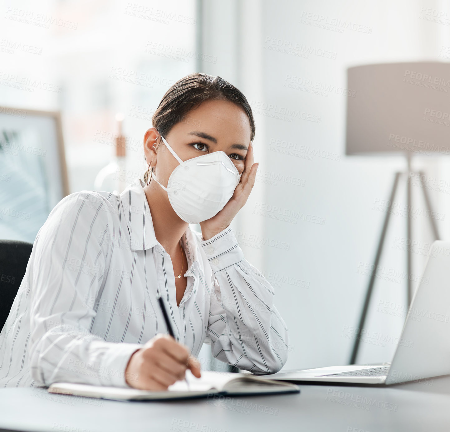Buy stock photo Shot of a masked young businesswoman looking unhappy while working at her desk in a modern office