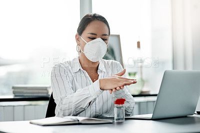 Buy stock photo Shot of a masked young businesswoman using hand sanitiser while working at her desk in a modern office