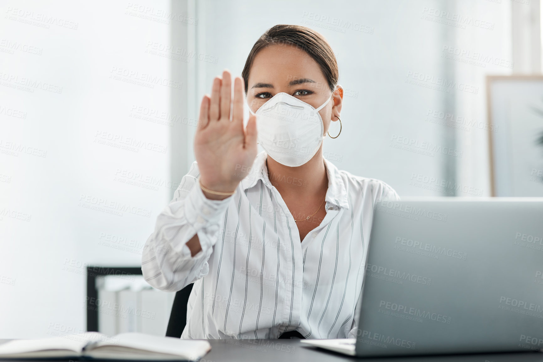 Buy stock photo Shot of a masked young businesswoman gesturing to stay away while working at her desk in a modern office