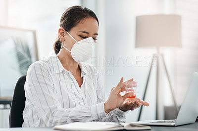 Buy stock photo Shot of a masked young businesswoman using hand sanitiser while working at her desk in a modern office