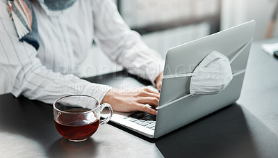 Buy stock photo Cropped shot of a businesswoman using a laptop with a mask wrapped around it and having herbal tea