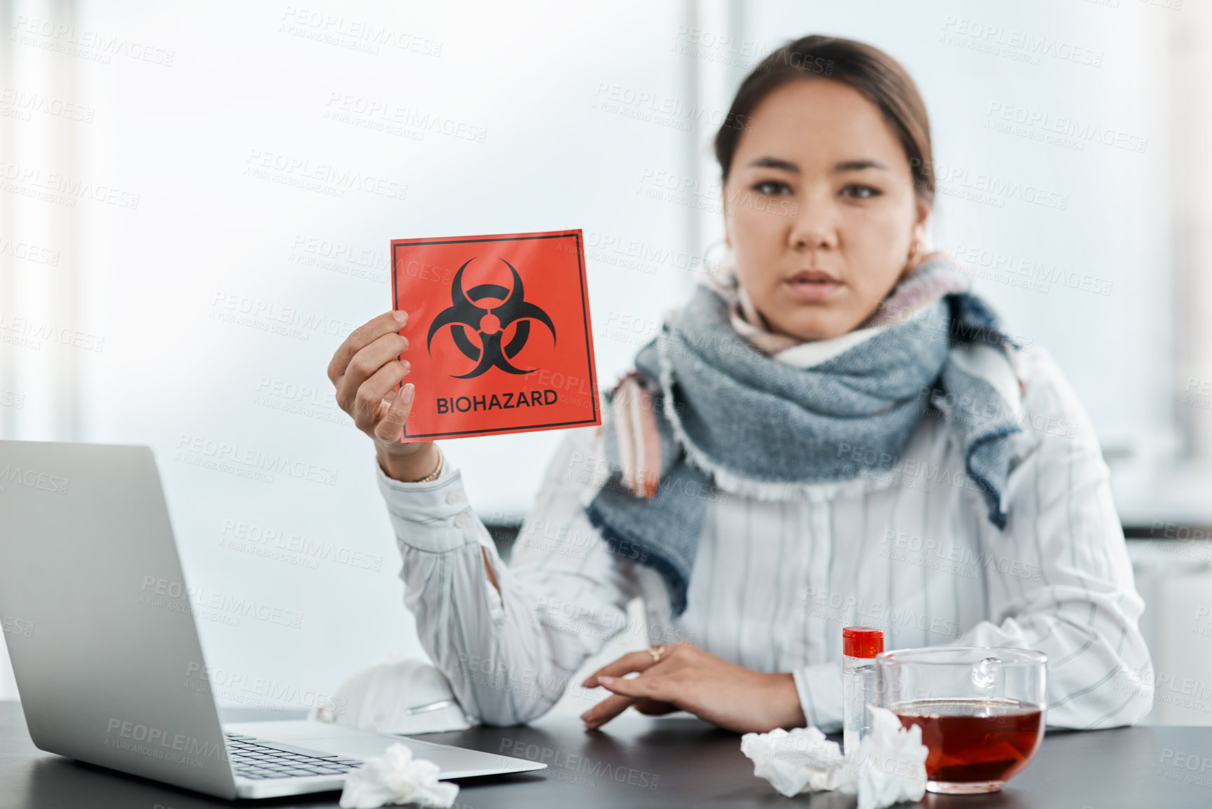 Buy stock photo Shot of a young businesswoman holding a biohazard sign at her desk in a modern office