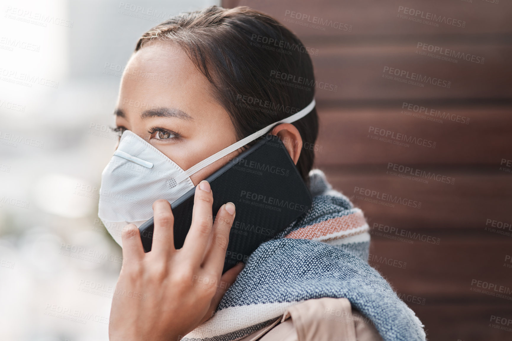 Buy stock photo Shot of a young woman wearing a mask while talking on the phone on the balcony at home