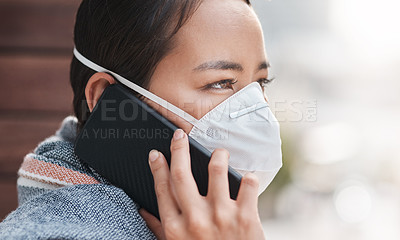 Buy stock photo Shot of a young woman wearing a mask while talking on the phone on the balcony at home