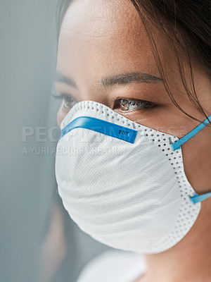 Buy stock photo Shot of a young woman wearing a mask while looking out a window at home