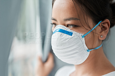 Buy stock photo Shot of a young woman wearing a mask while looking out a window at home