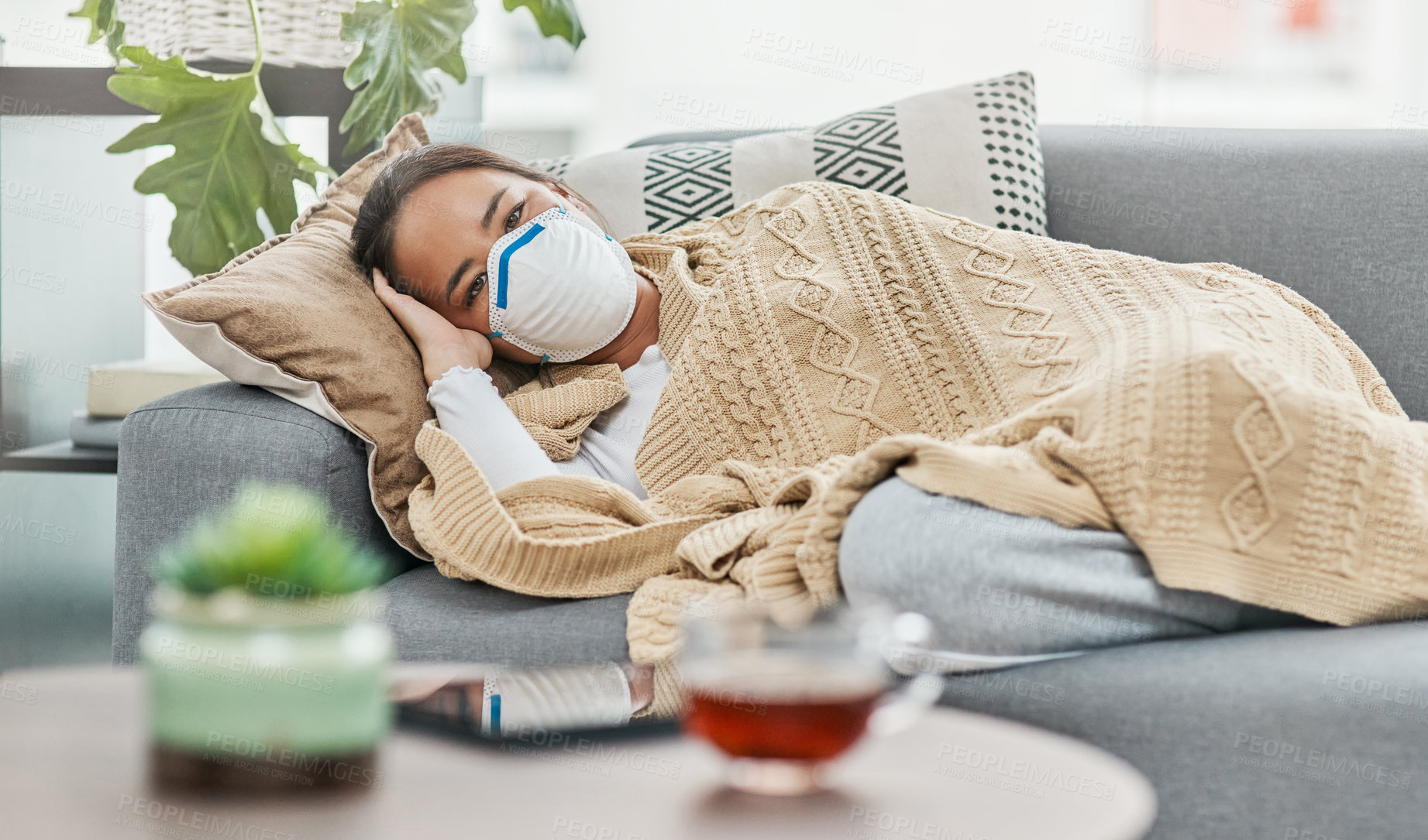 Buy stock photo Shot of a woman wearing a mask while lying sick at home