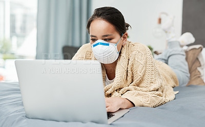 Buy stock photo Shot of a woman wearing a mask while lying on her bed with her laptop
