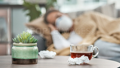 Buy stock photo Shot of dirty tissues and a cup of tea on a table next to a woman lying sick at home