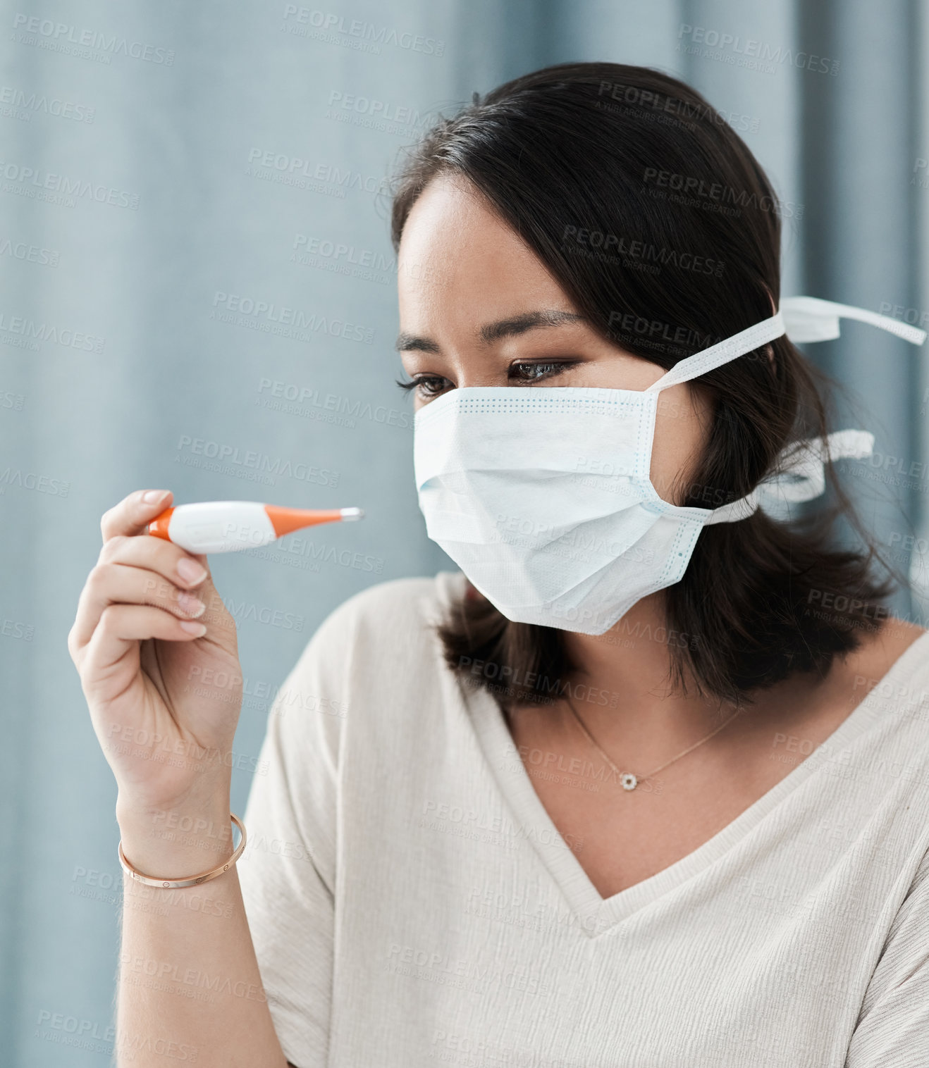 Buy stock photo Shot of a woman wearing a mask while checking her temperature at home