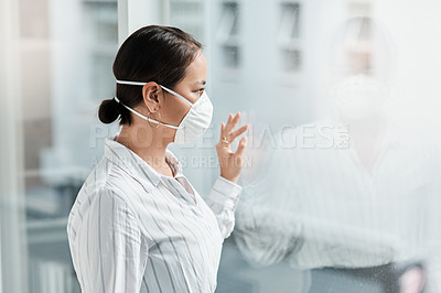 Buy stock photo Shot of a masked young businesswoman looking out of a window and waving in a modern office