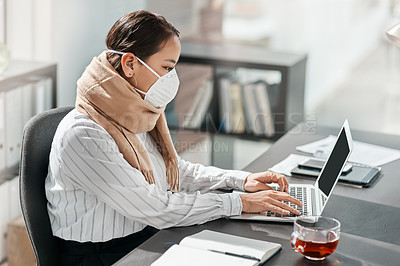 Buy stock photo Shot of a masked young businesswoman using a laptop at her desk in a modern office