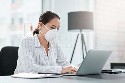 Buy stock photo Shot of a masked young businesswoman working at her desk in a modern office