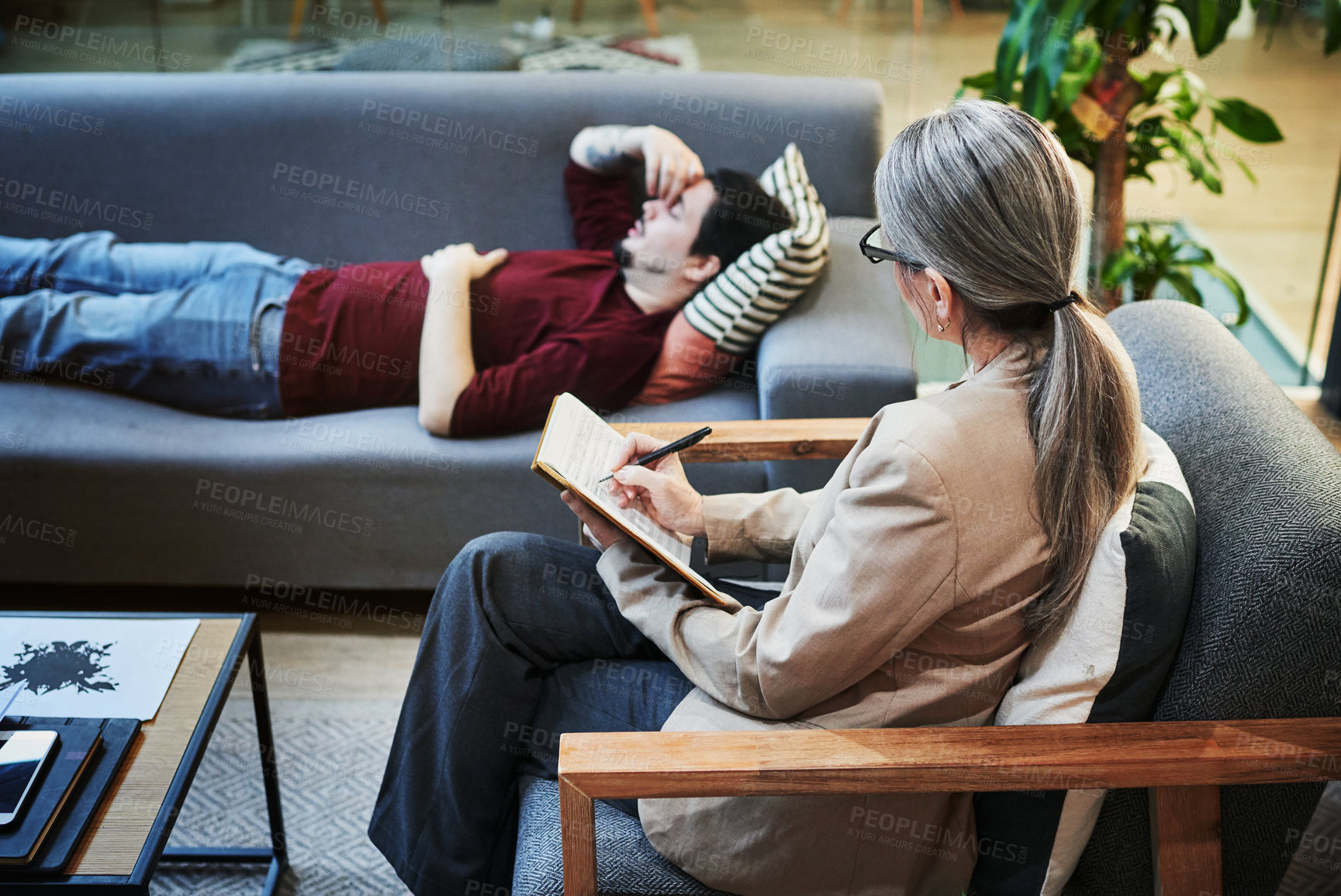 Buy stock photo Shot of a young man having a therapeutic session with a psychologist and looking upset