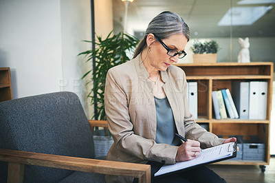 Buy stock photo Shot of a mature psychologist writing notes on a clipboard