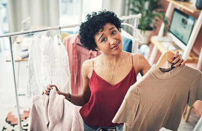 Buy stock photo Cropped shot of a young woman holding up two clothing items while looking at the camera