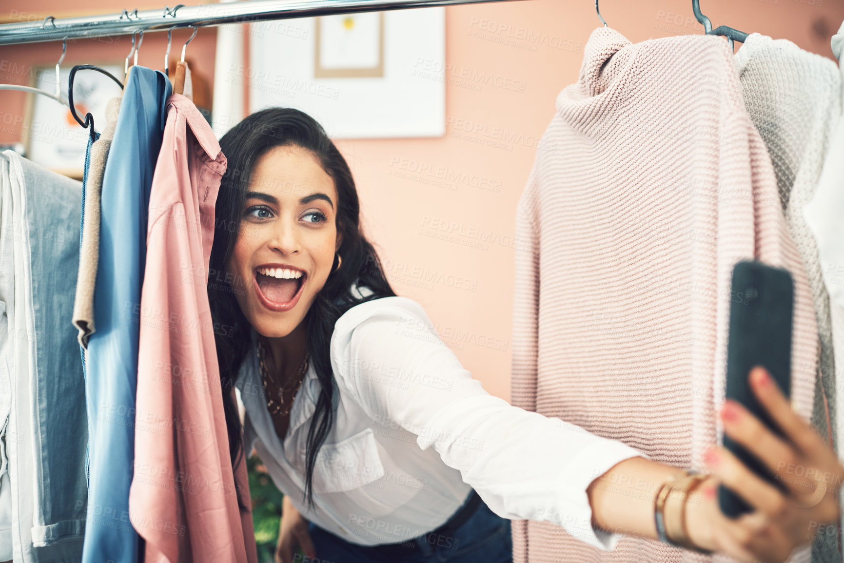 Buy stock photo Shot of a woman sticking her head in between items on a clothing rail while taking a selfie