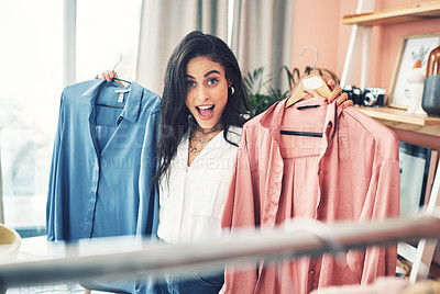 Buy stock photo Cropped shot of a young woman holding up two clothing items while looking at the camera