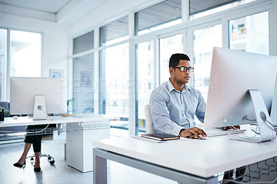 Buy stock photo Shot of a young businessman using a computer in a modern office