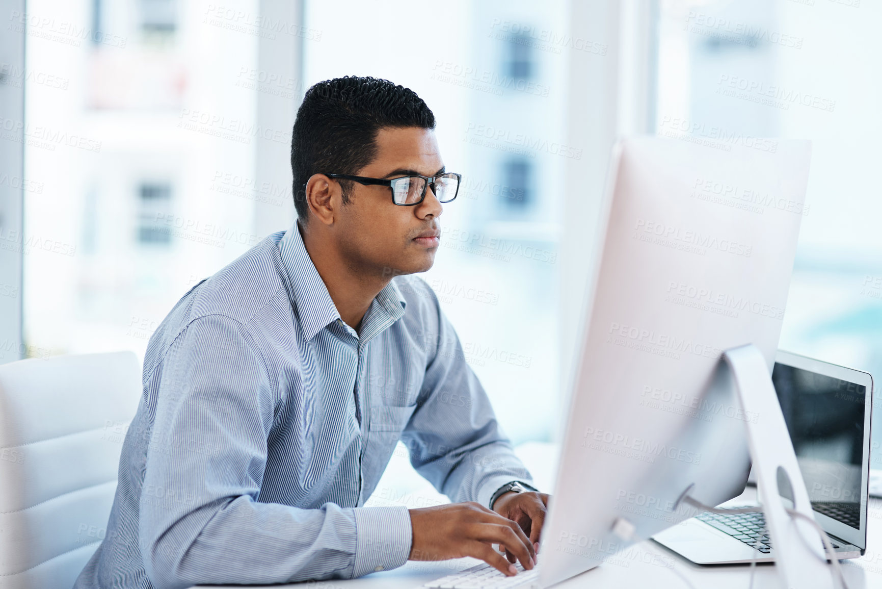 Buy stock photo Shot of a young businessman using a computer in a modern office