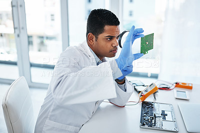 Buy stock photo Shot of a young man using a magnifying glass while repairing computer hardware in a laboratory