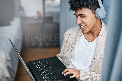 Buy stock photo Shot of a young man using a laptop and headphones at home