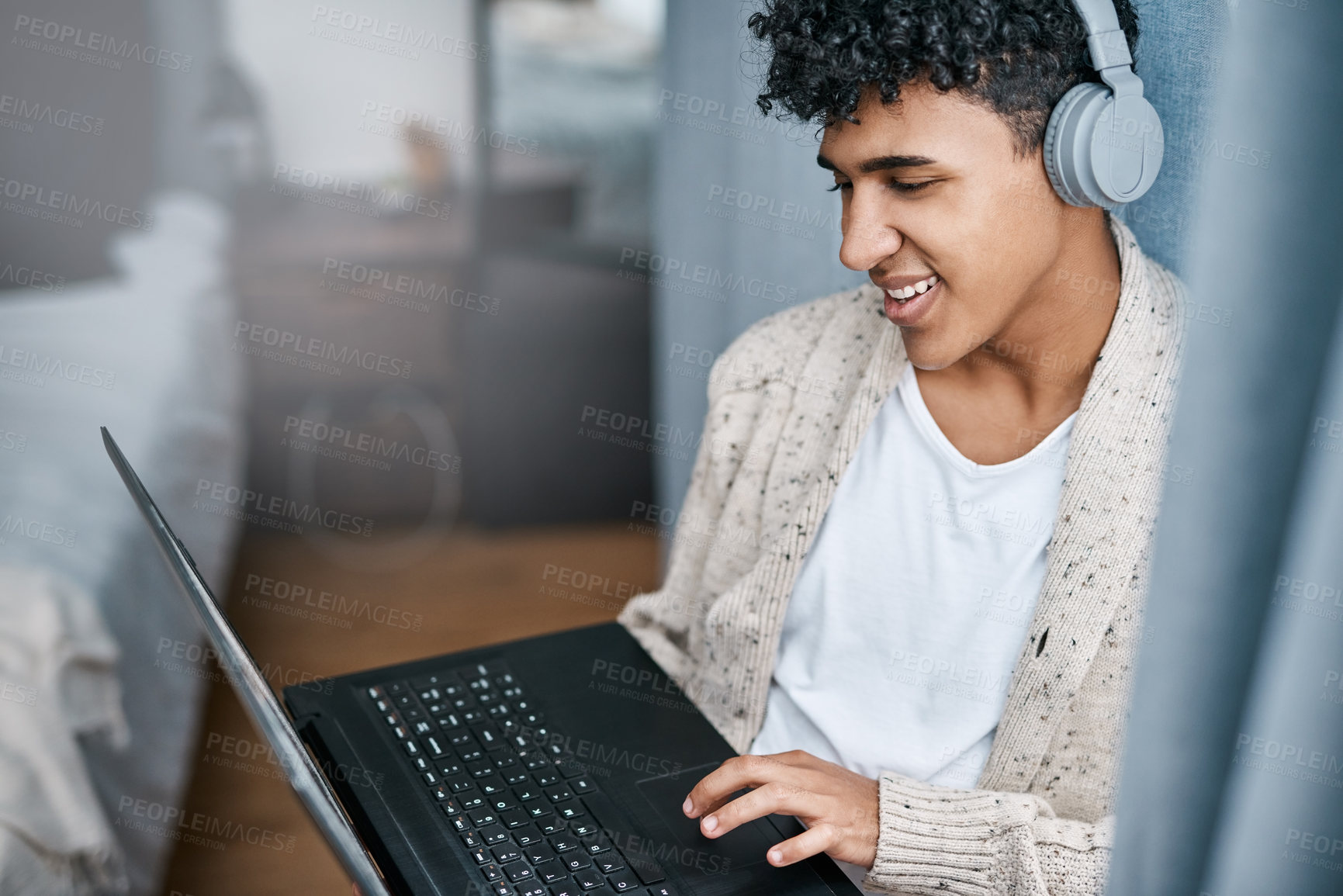 Buy stock photo Shot of a young man using a laptop and headphones at home