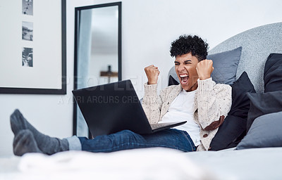 Buy stock photo Shot of a young man cheering while using a laptop on his bed at home