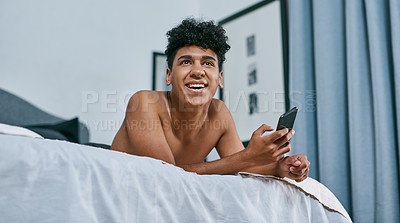 Buy stock photo Shot of a young man relaxing on his bed and using a smartphone