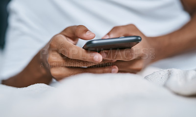 Buy stock photo Cropped shot of a man relaxing on his bed and using a smartphone
