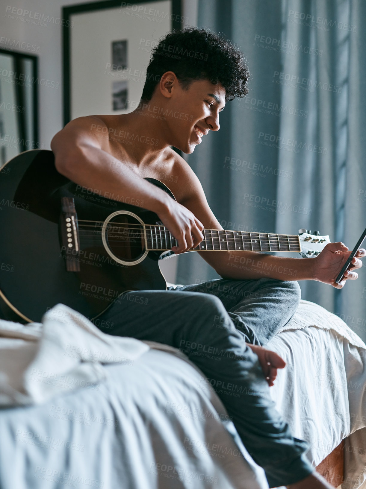 Buy stock photo Shot of a young man using a smartphone while playing the guitar at home
