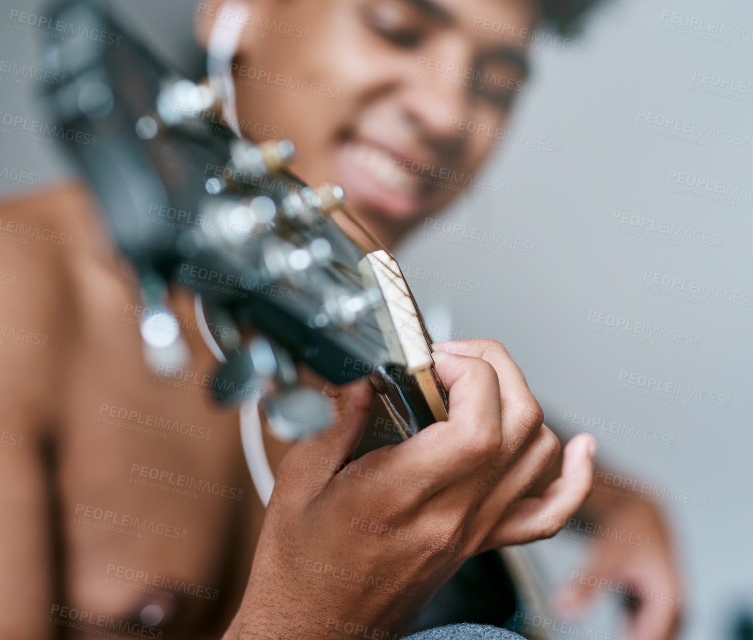 Buy stock photo Shot of a young man using earbuds while playing the guitar at home