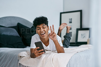 Buy stock photo Shot of a young man using a smartphone while relaxing on his bed at home