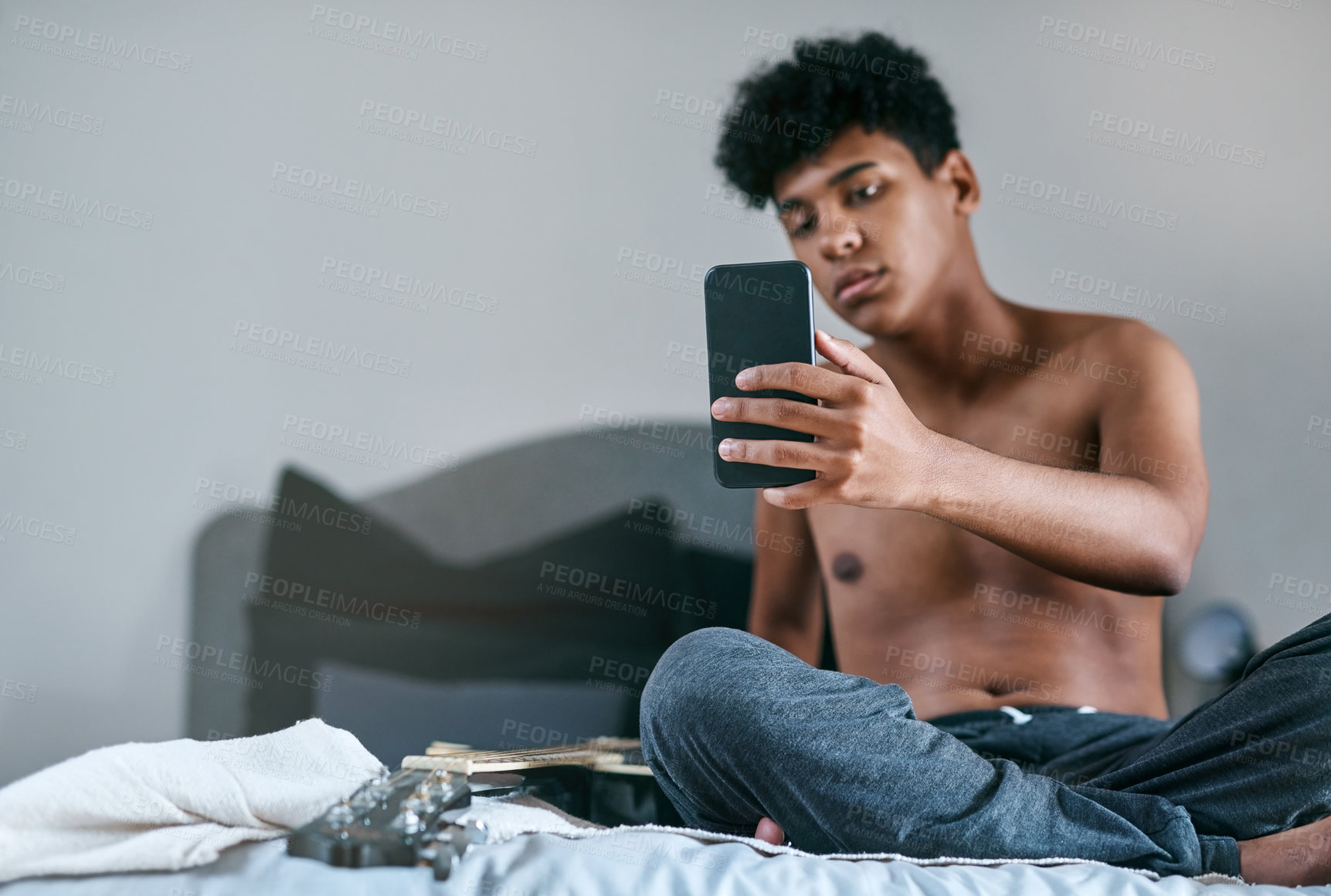 Buy stock photo Shot of a young man relaxing on his bed and taking selfies with a smartphone