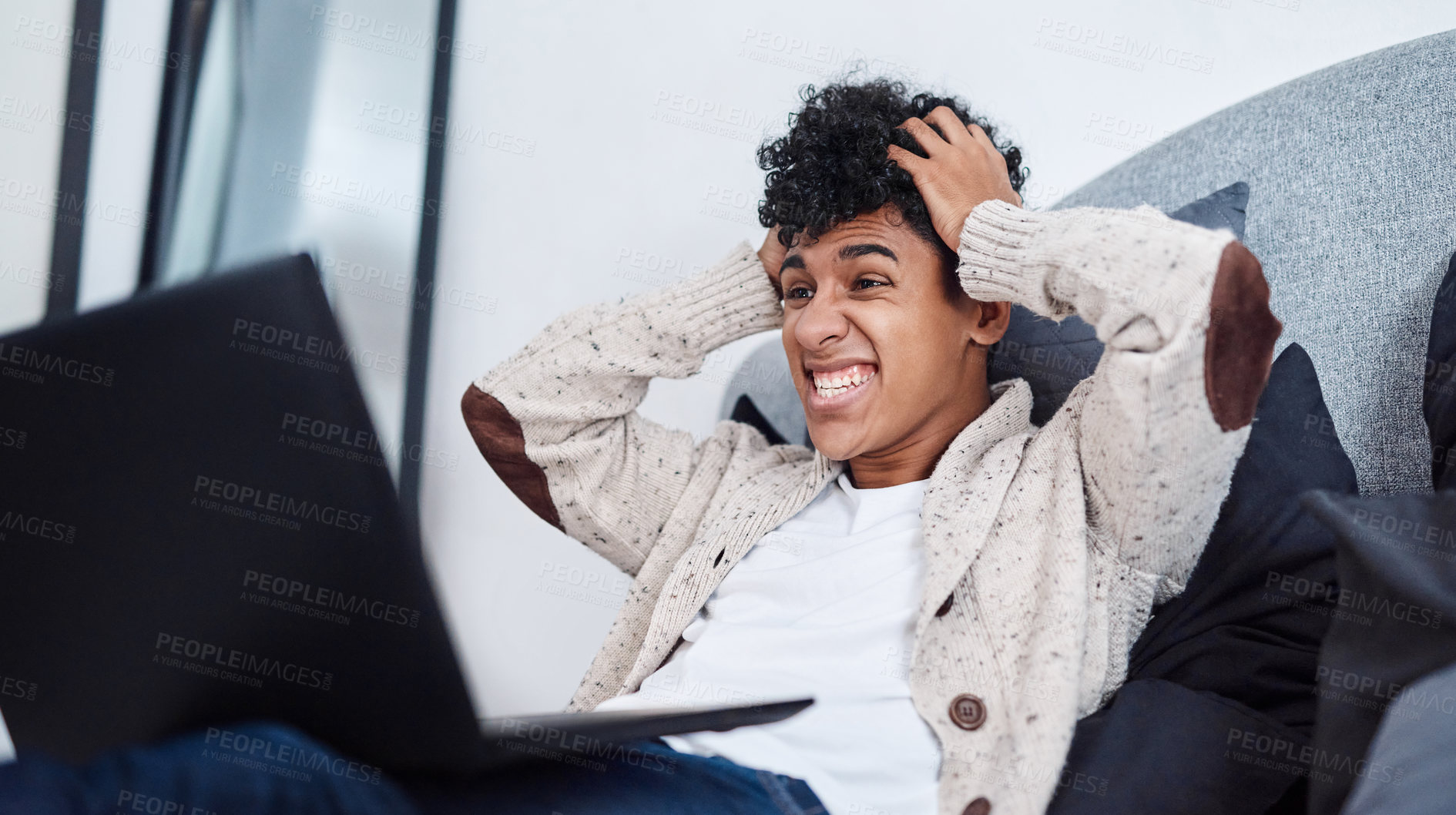 Buy stock photo Shot of a young man looking shocked while using a laptop on his bed at home