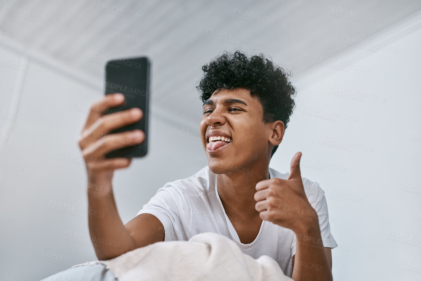 Buy stock photo Shot of a young man using a smartphone while relaxing on his bed at home