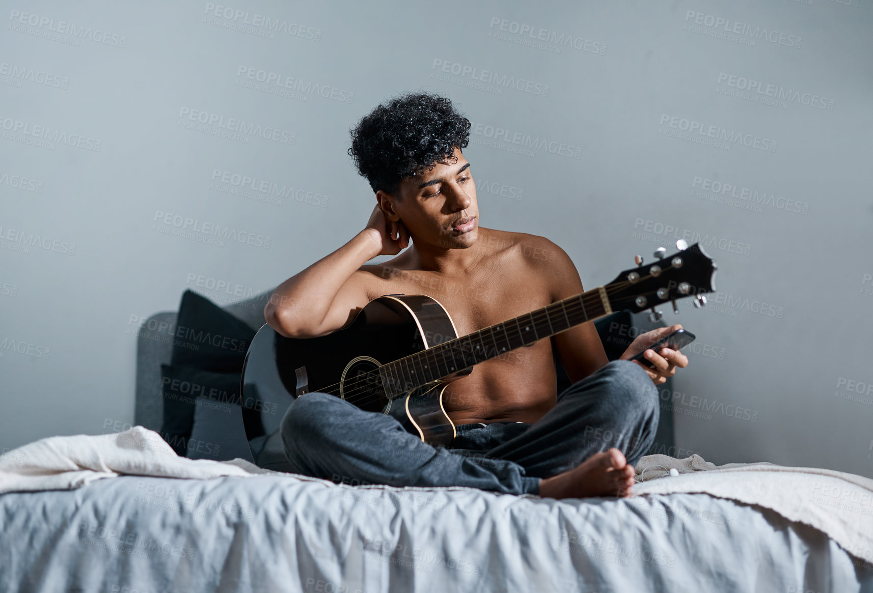 Buy stock photo Shot of a young man using a smartphone while playing the guitar at home