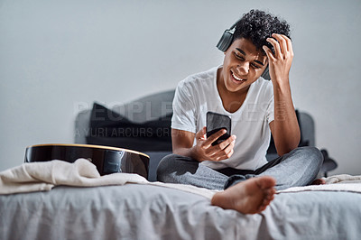 Buy stock photo Shot of a young man using a smartphone and headphones to listen to music at home