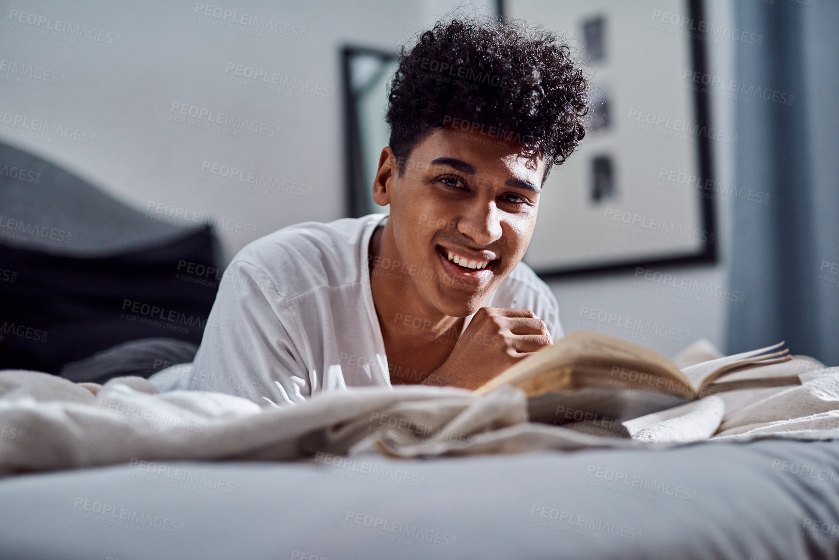 Buy stock photo Shot of a young man reading a book and relaxing on his bed at home