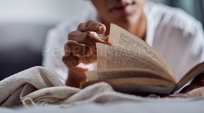 Buy stock photo Cropped shot of a young man reading a book and relaxing on his bed at home