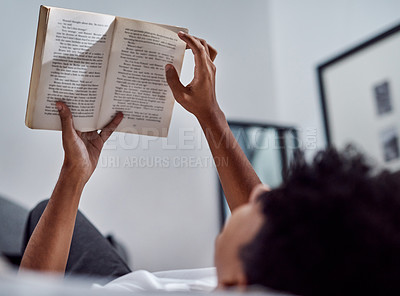 Buy stock photo Cropped shot of a young man reading a book and relaxing on his bed at home