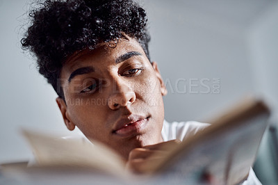 Buy stock photo Shot of a young man reading a book and relaxing on his bed at home